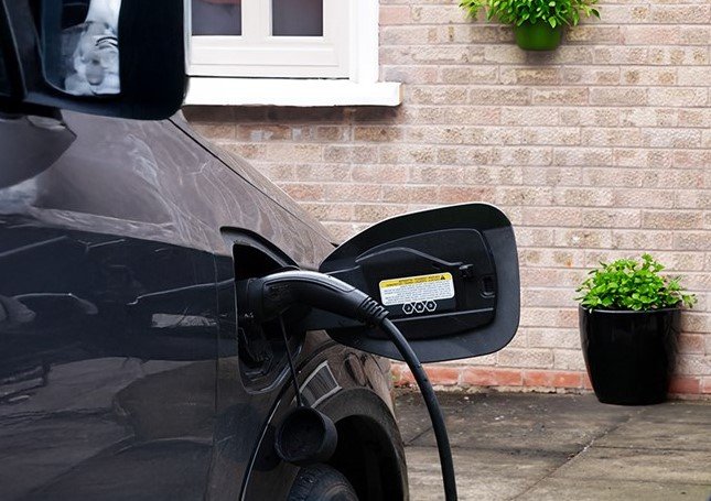 Electric car charging at home, connector plugged in next to a brick wall